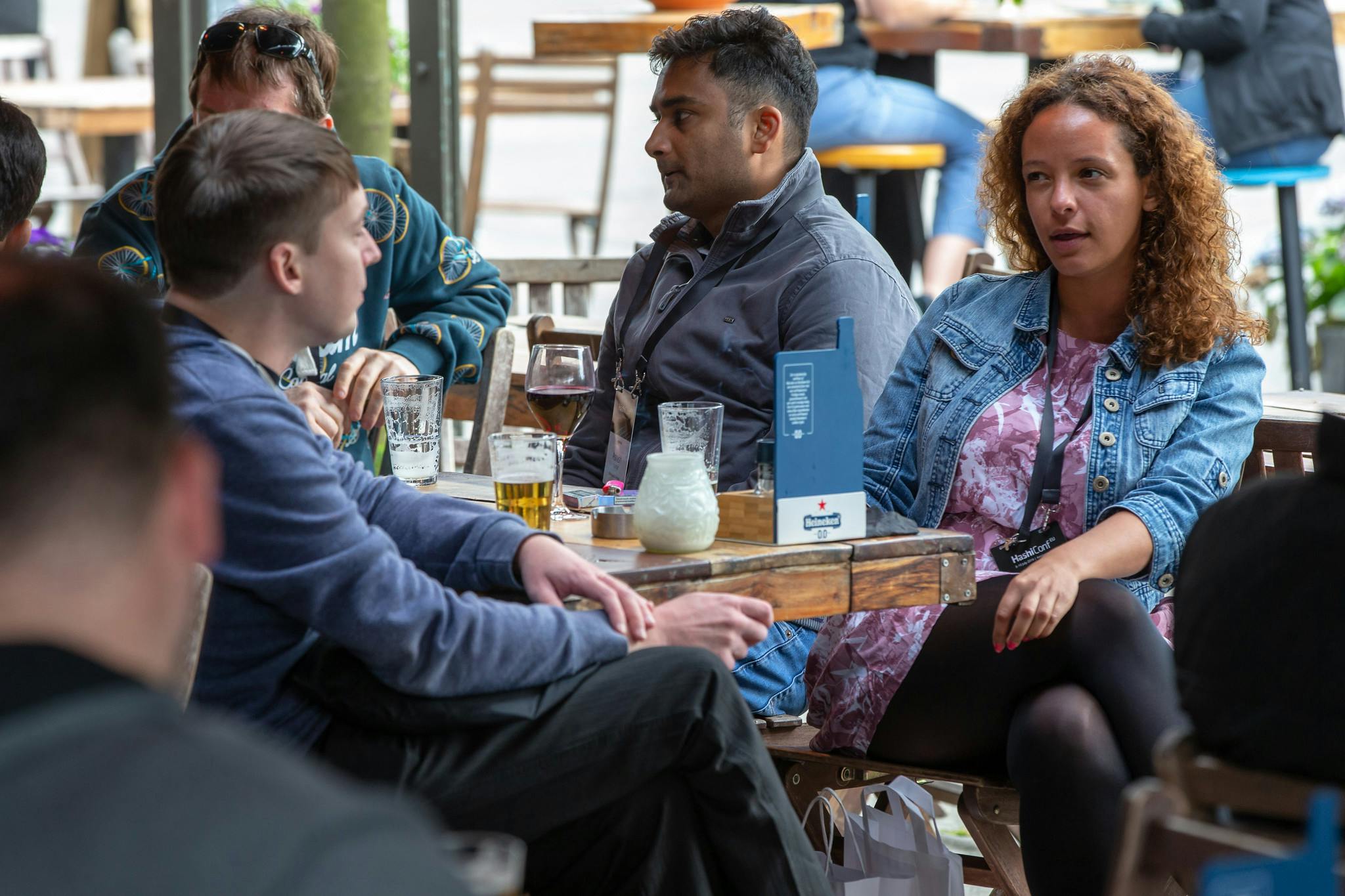 Photograph from HashiConf Eu 2019. People are seated around a table. A woman with shoulder length curly brown hair wearing a denim jacket and pink shirt is seated across from a man with short brown hair wearing a long sleeve dark blue shirt.